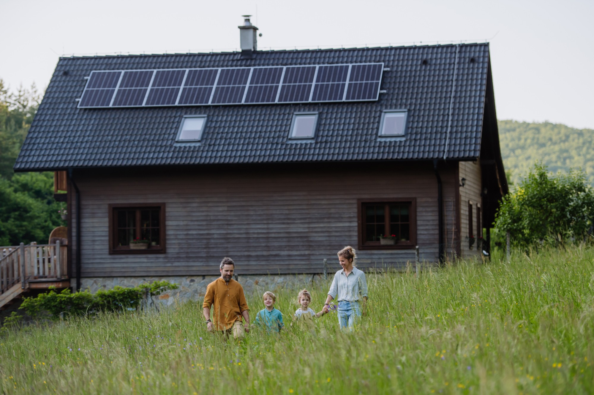 Familj går över ängen framför sitt trähus med solceller på taket
