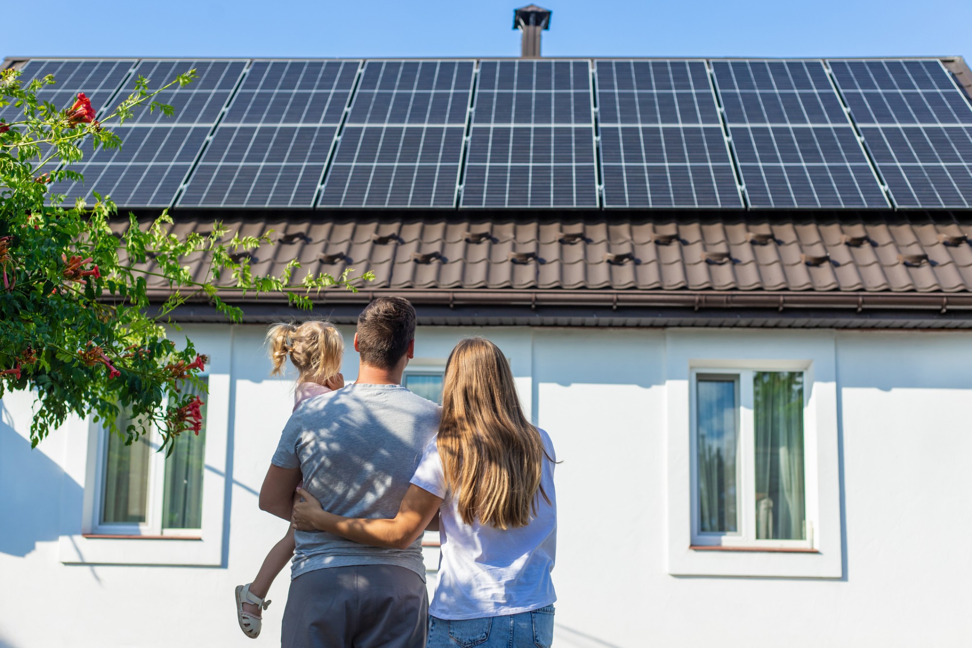 Familj står framför sitt hus och tittar upp på solcellerna
