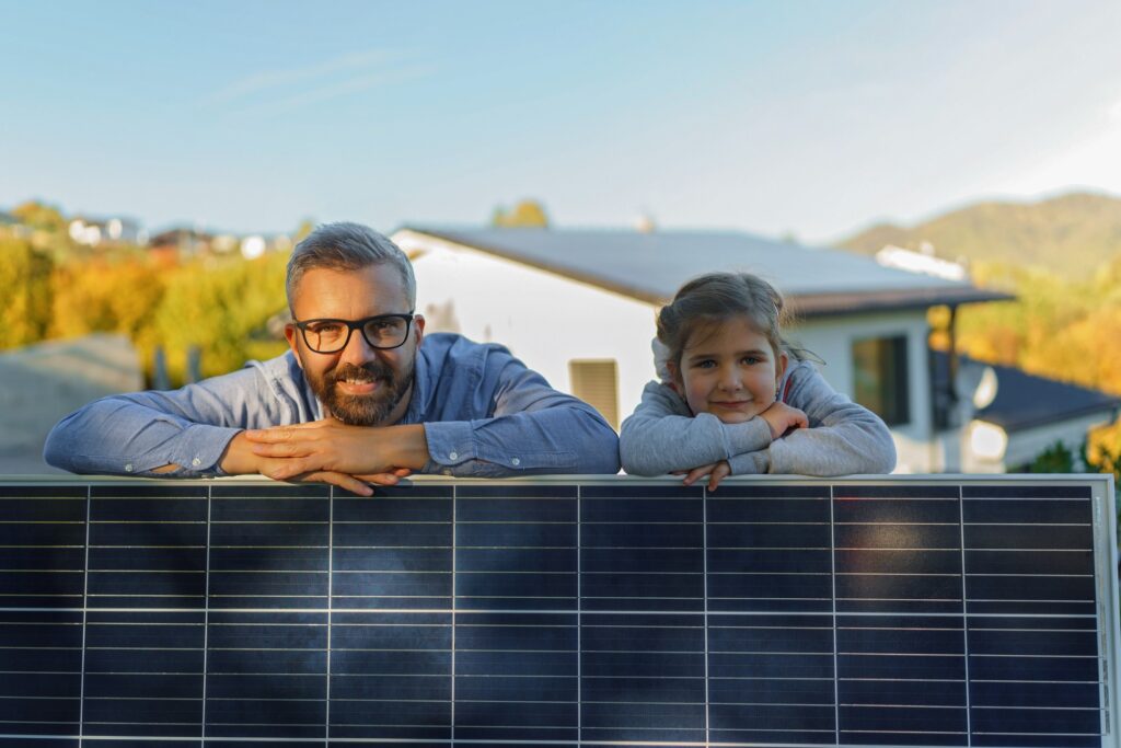 Pappa och dotter lutar sig mot en solpanel framför sitt hus