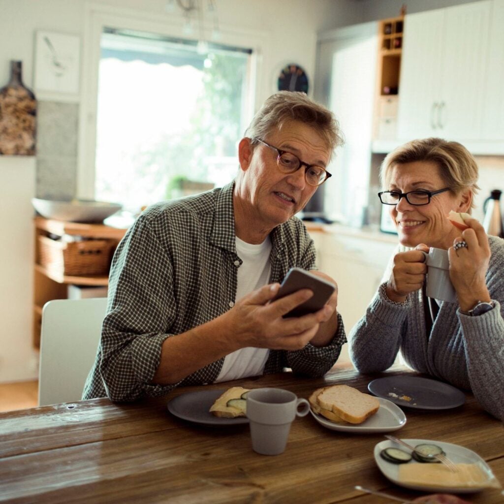 Par sitter vid köksbordet och tittar på en batterioffert i mobilen.