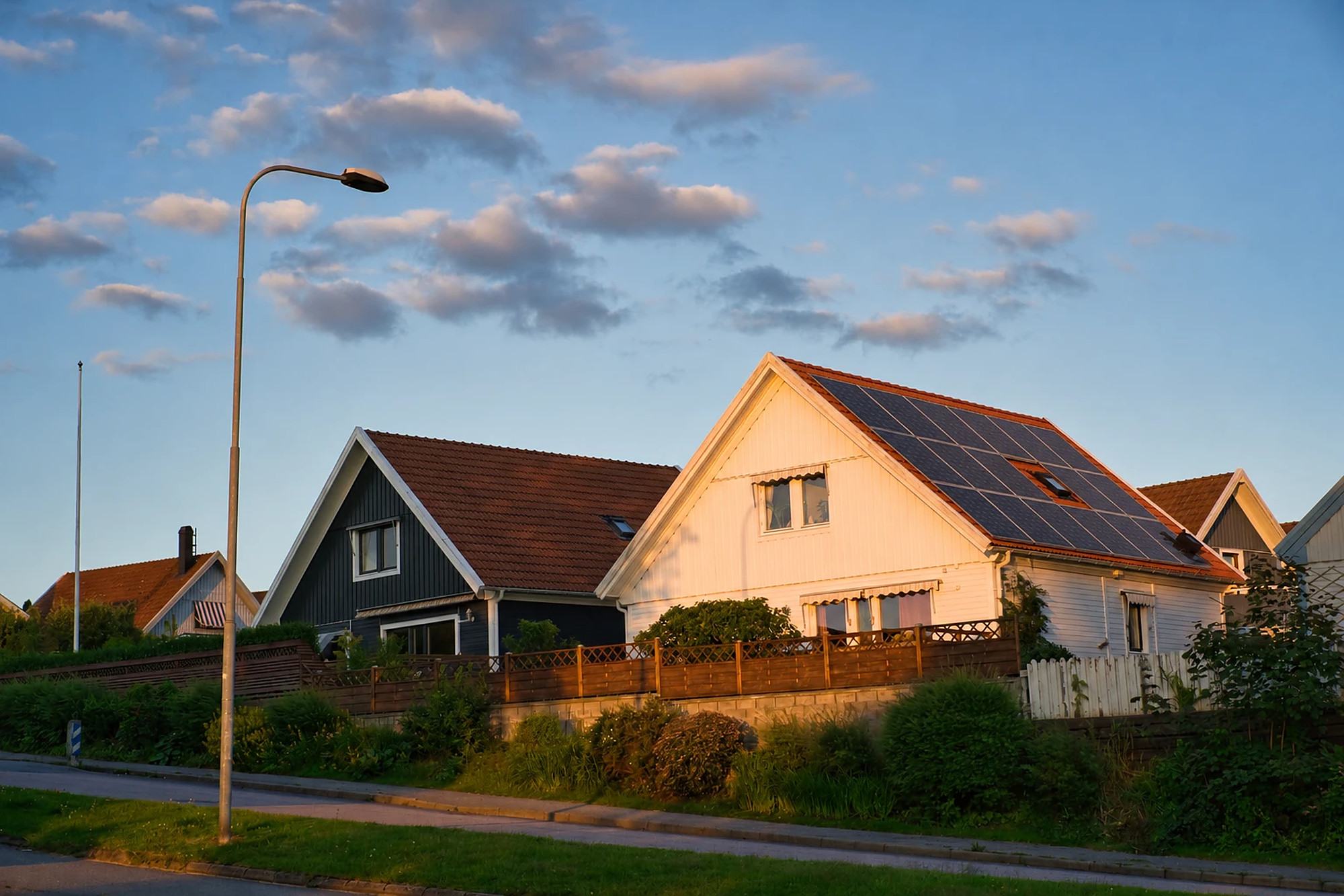 Vit villa med solceller på taket i kvällssol, sedd från gatan.