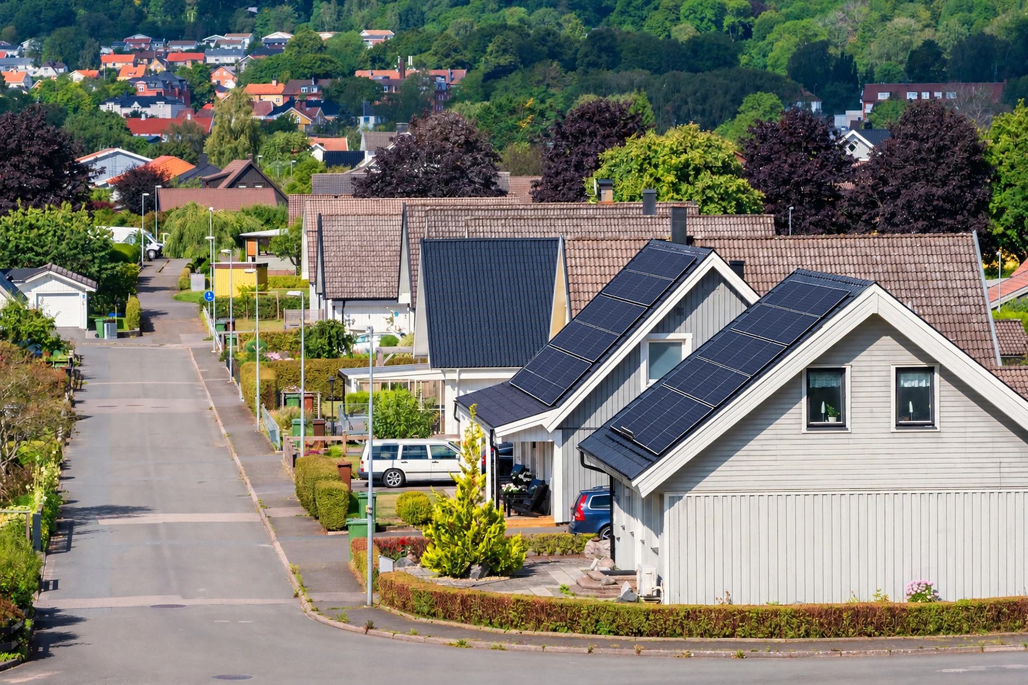 Grå villa med svarta solceller på taket längs en villagata med fler hus bakom.